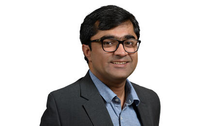 Mustafa Naseem wearing a suit and glasses and smiling at the camera.