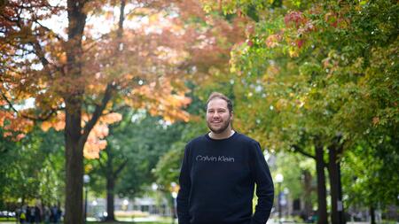 A photo of Joey Quick standing on campus with fall foliage behind him.