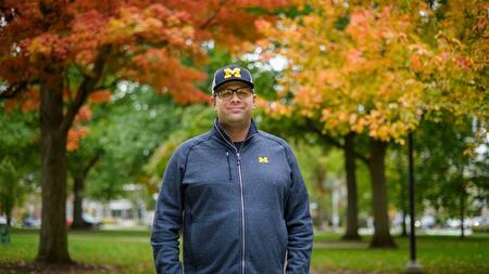 A photo of Kyle Bylin standing on campus with fall foliage behind him.
