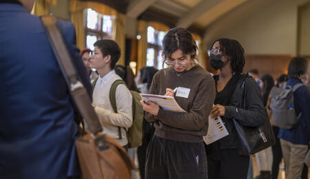A student stands in line at the UMSI career fair, holding a folder and making notes with a pencil.