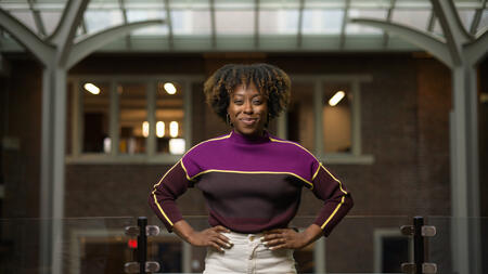 Robin Brewer stands with both her arms at her hips, wearing a sweater and smiling into the camera. 