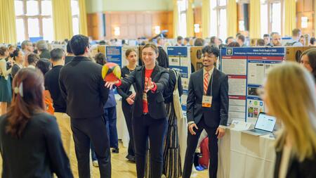 Students standing in front of a trifold display in the ballroom of the Michigan League toss around a rugby ball 