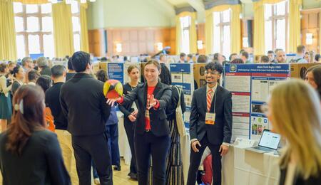 Students standing in front of a trifold display in the ballroom of the Michigan League toss around a rugby ball