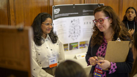 An alumna wearing a judge badge speaks to a student in the Michigan League during UMSI's student project exposition