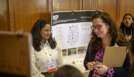 An alumna wearing a judge badge speaks to a student in the Michigan League during UMSI's student project exposition
