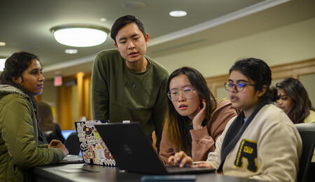 Three students looking at a laptop together in a classroom