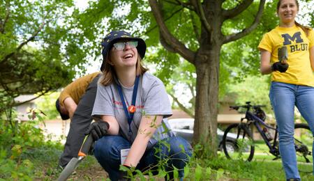 A UMSI student holds a shovel and smiles while working in a rain garden