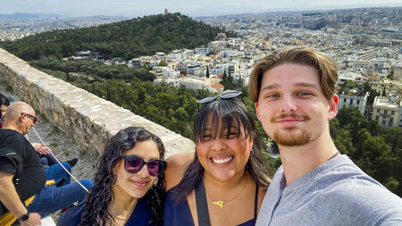 Three people taking a selfie overlooking a forest and a city