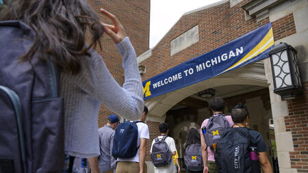 A photo of students wearing UMSI backpacks walking toward an arch with a University of Michigan banner clearly displayed at the entrance