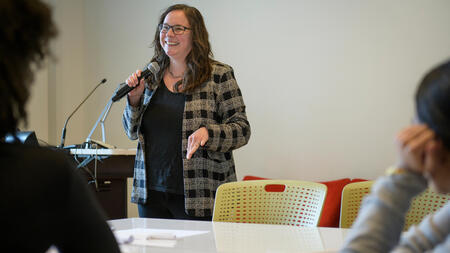 Dean Andrea Forte holds a microphone and stands in the front of a classroom.