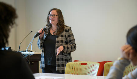 Dean Andrea Forte holds a microphone and stands in the front of a classroom.