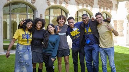 Seven CCSI fellows pose on the grass outside of North Quad, smiling and holding up peace signs