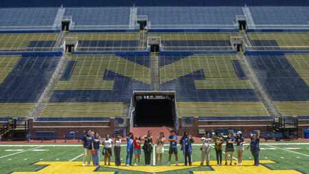 A far-off shot of high school students standing on the field at Michigan Stadium, posed over the block M