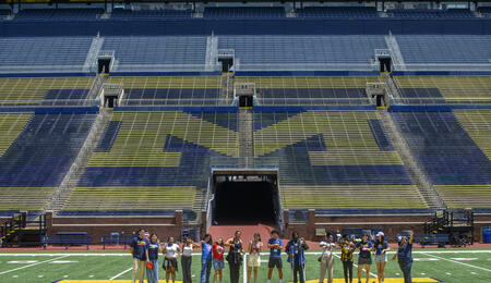 A far-off shot of high school students standing on the field at Michigan Stadium, posed over the block M