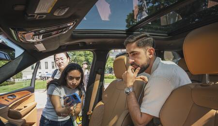 An interior view of a vehicle as three UMSI students study the user interface, with one taking a photo on their cell phone