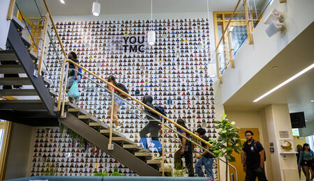 A side view of an open, modern staircase with high school students climbing up it, wearing backpacks
