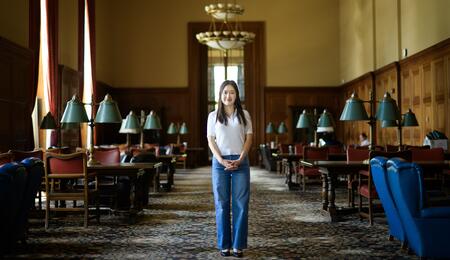 Jane Im stands in a carpeted room in Rackham with dark wood tables lining either side