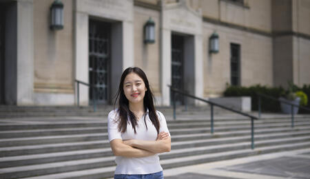 Jane Im stands in front of an academic building, arms crossed in front of her