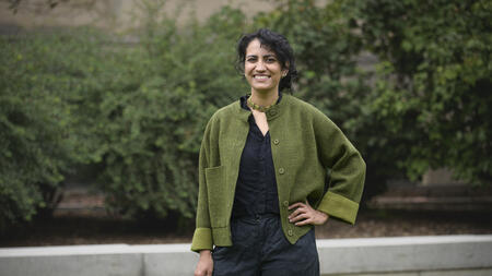 Amina Abdu smiles into the camera while standing outside wearing a green cardigan. 