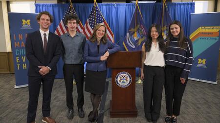 Secretary of State Jocelyn Benson poses for a photo with Jackson Gelbard, Dylan Siewert, Susan Cheng and Kathleen Andonian, standing on either side of a podium 