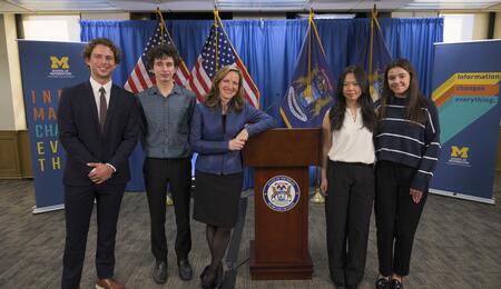 Secretary of State Jocelyn Benson poses for a photo with Jackson Gelbard, Dylan Siewert, Susan Cheng and Kathleen Andonian, standing on either side of a podium
