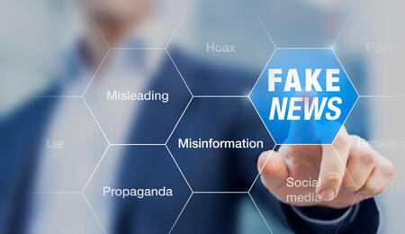 A photo of a man in a suit clicking on a clear screen with a variety of bubbles that read misleading, propaganda, deception and fake news.