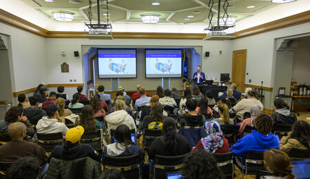 Ben Marchionna stands in front of a presentation screen speaking with a crowded room