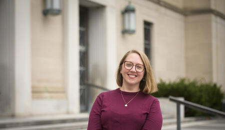 Rebecca Frank wearing a maroon sweater, a neckplace and glasses and smiling at the camera.