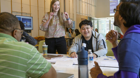 Career coach Jordan Hansen gestures excitedly at a table with three students 