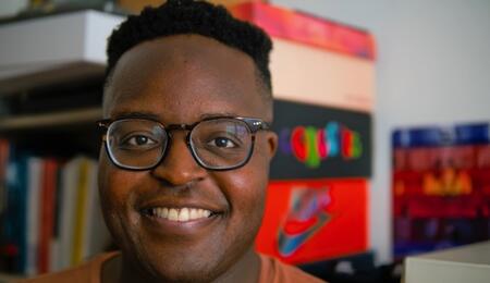 A headshot of Hope Tambala with colorful shelves and file boxes visible behind him