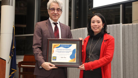 Arthur Lupia and Julie Hui stand next to each other holding Julie's award and smiling into the camera. 