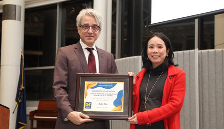 Arthur Lupia and Julie Hui stand next to each other holding Julie's award and smiling into the camera.