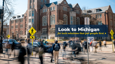 A graphic with a logo that says "Look to Michigan for tech solutions that put people first" over an image of students crossing State Street in front of the Michigan Union on a clear spring day. The students give the illusion of moving very quickly as a result of a long exposure photo, causing them to all have a heavy trail of motion blur.