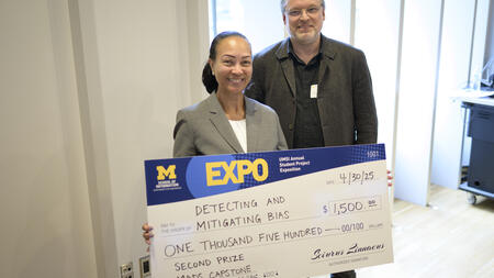 Celia Banks poses, smiling, beside Kevyn Collins-Thompson, holding an award check with an Expo and UMSI logo
