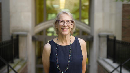 A headshot of Elizabeth Yakel posing in front of the glass entrance to a building, smiling in a navy linen blouse 