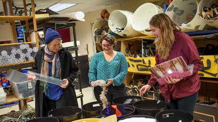 Three people sorting craft supplies in a room full of buckets.