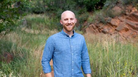 Dane Jacobsen smiling outdoors in a grassy landscape featuring craggy rock face.