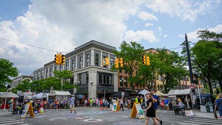 Downtown Ann Arbor during a street fair. There are tents lining the streets and chalk art on the ground.