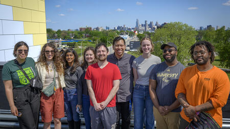Eight students and Matt Bui pose on the rooftop of the LOVE Building with the Detroit skyline behind them