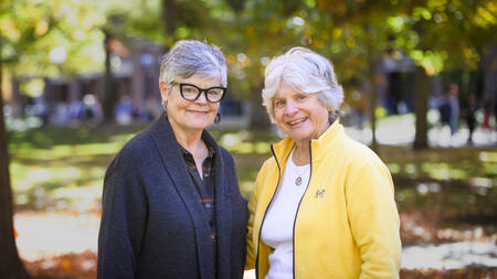Kenlee Ray and Sue Quackenbush smiling on an autumnal quad wearing dark blue and maize 