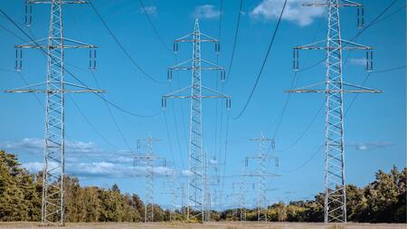 Multiple tall metal electricity transmission towers stretch across an open rural landscape, connected by overhead power lines.