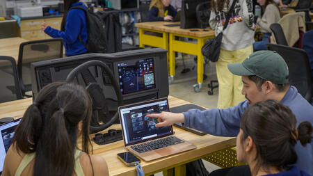 Three people face a computer screen and car dashboard prototype, as one collaboratively points to an element on-screen