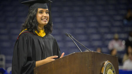 Sonia Doshi speaks at a podium wearing regalia 