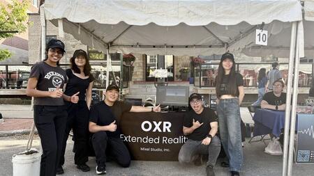 Five people pose at a booth with a table cover that says OXR Extended Reality