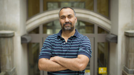 Joyojeet Pal stands outside cross armed in a striped blue shirt. 