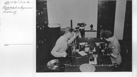A black and white photo shows Dorothy Arbaugh inspecting motion picture film, seated across from someone else at a table