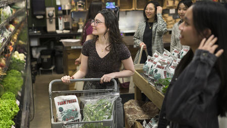 A group of students in a grocery store. One is using a cart. 