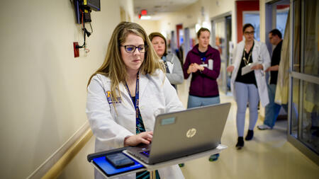 A person in a white doctor coat using a laptop in a hospital