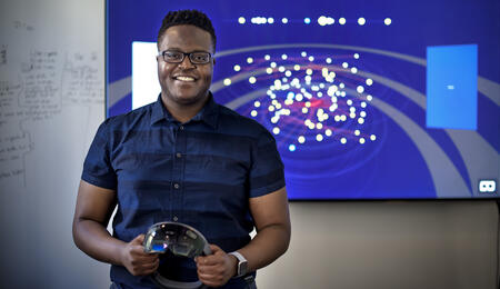 Hope Tambala standing in front of a data visualization holding VR glasses.