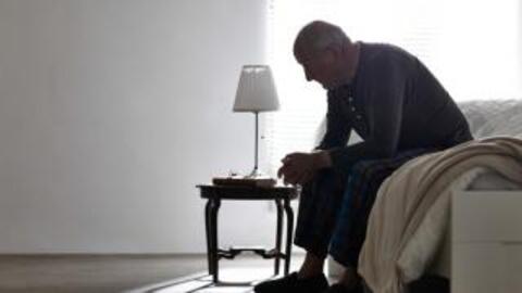 An elderly man sitting on the edge of the bed.